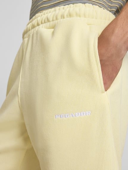 Männermodel draagt Relaxed Fit Shorts met structuurpatroon Model 'Lagos' van Pegador in lichtgeel, elastische materiaalmix, elastische band, detailopname voorkant, context: Heren korte broek van Pegador, relaxed fit, bandwijdte maat M 38 cm, binnenbeenlengte maat M 21 cm.