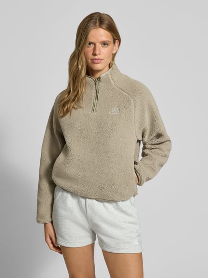 Frauenmodel trägt Regular Fit Fleecejacke mit Stehkragen von adidas Sportswear in Beige, weiche Textur, Ganzkörperansicht von vorne.
