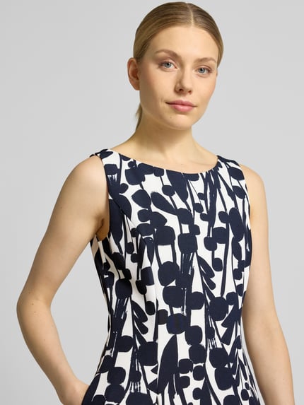 Kobiece modelka nosi knielanges Cocktailkleid mit Nahtreißverschluss von Vera Mont, elastyczna mieszanka materiałów, krój slim fit, asymetryczny dekolt w serek, wszyty zamek błyskawiczny, z krótkim rękawem, marszczone fałdy, długość do kolan, długość tyłu w rozmiarze 36: 99 cm, szerokość w rozmiarze 36: 43 cm, wzór w granatowe i białe abstrakcyjne kształty, widok z przodu, zbliżenie na górną część ciała