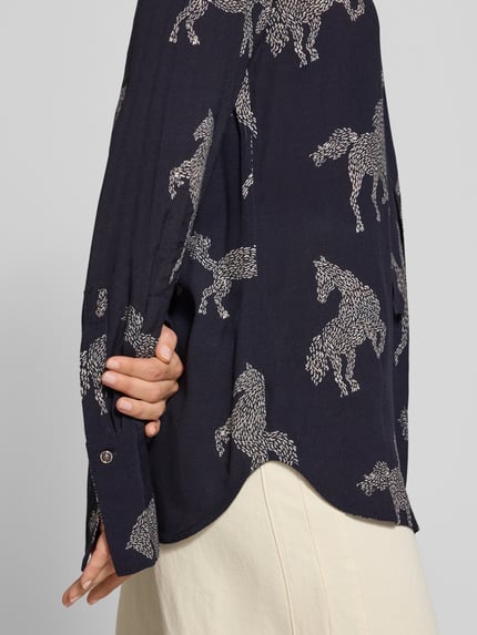 Frauenmodel trägt Relaxed Fit Bluse aus reiner Viskose Modell 'ODETTA' von ODETTA, dunkelblau mit weißem Allover-Motiv-Print, Zierschleife, langärmeliges Design, strukturierte Stoffoberfläche, Nahaufnahme Oberkörper.