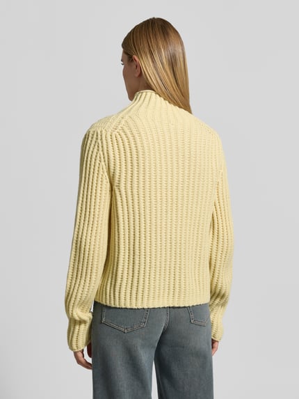 Frauenmodel trägt Strickpullover mit Stehkragen Modell 'ARWIE' von DRYKORN, gelb, gerippte Textur, Regular Fit, Rückansicht, Material-Mix mit Alpaka-Anteil.