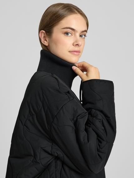 Vrouwenmodel draagt zwarte gewatteerd jack met doorgestikte naden, gebreide opstaande kraag en steekzakken, Model 'SERENA' van JJXX, loose fit, ritssluiting, Nahaufnahme Oberkörper.