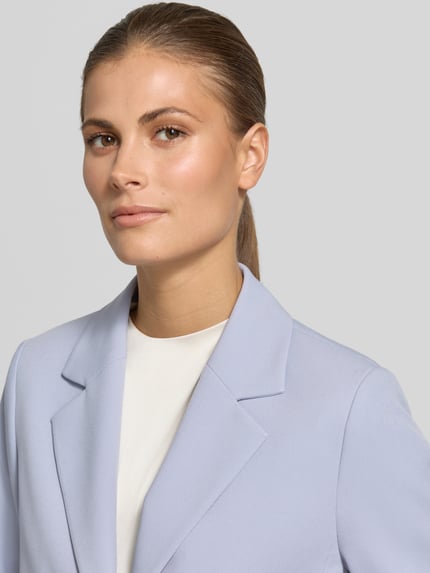 Frauenmodel trägt Regular Fit Kurzblazer mit 1-Knopf-Verschluss von s.Oliver BLACK LABEL, Optik: Unifarben, Reverskragen, Langarm, Ärmelabschluss: Geschlitzt, Nahaufnahme Oberkörper.