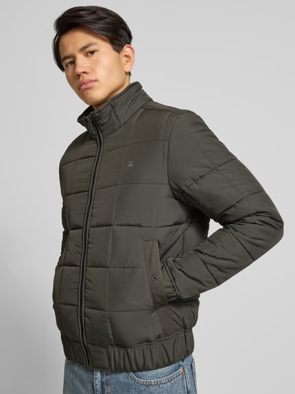 Männermodel trägt Steppjacke mit Reißverschluss von G-Star in Dunkelgrün, Regular-Fit, Stehkragen, Label-Print, Eingrifftaschen, elastische Abschlüsse, Ganzkörperansicht von vorne.