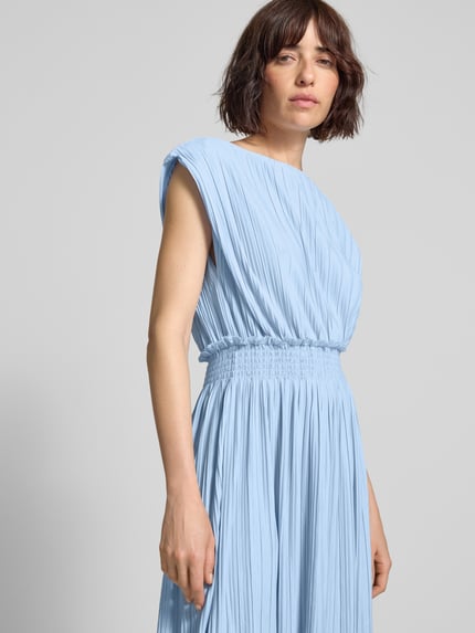 Modelka nosi długą sukienkę Maxikleid mit Plisseefalten und rückseitiger Schnürung von ICHI z mieszanki materiałów z dodatkiem streczu, taliowany krój, model 'YAMILET', dekolt w łódkę, plisy, marszczone detale, wiązanie z tyłu, długość tyłu w rozmiarze S 121 cm, szerokość w rozmiarze S 45 cm, jasnoniebieski kolor, tekstura plisowana. Zbliżenie na górną część ciała z przodu.