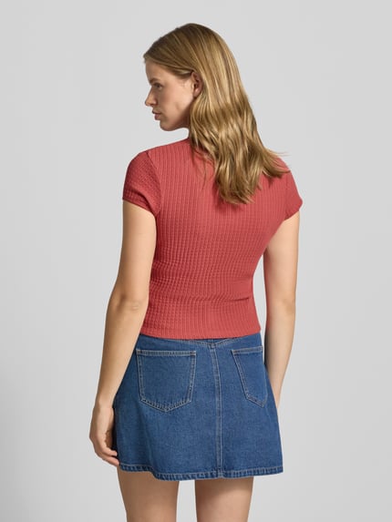 Vrouwenmodel draagt Slim Fit T-shirt met doorlopende knoopsluiting model 'AJOUR' van REVIEW uit puur katoen; ruglengte maat S 49 cm; korte mouw, ronde hals; denim rok; rugaanzicht.