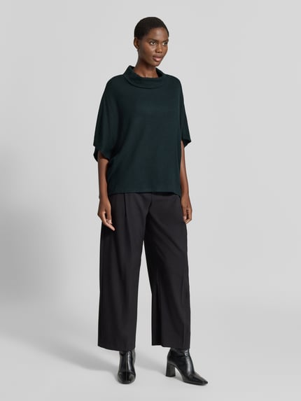 Kobiece modelka nosi sweter z dzianiny 'Strickpullover aus Viskose-Mix mit 1/2-Arm' od Apricot, mieszanka wiskozy z dodatkiem streczu, krój relaxed fit, golf, rękaw o dł. 1/2, długość tyłu w rozmiarze S: 61 cm, długość rękawów: 27 cm, ciemny zielony kolor, gładka faktura, pełny widok z przodu.