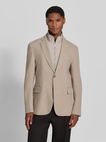 Męski model nosi Slim Fit Sakko mit Viskose-Anteil von Manuel Ritz, jasnobeżowy, Mieszanka materiałów z dodatkiem wiskozy, Stójka z zamkiem błyskawicznym, Kołnierz z połami, Brustasza, listwa guzikowa, kieszenie z patką, Długość tyłu w rozmiarze 50: 78 cm, Szerokość w rozmiarze 50: 44 cm, Długość rękawów w rozmiarze 50: 68 cm, widok całej sylwetki z przodu.