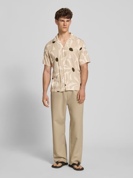 Männermodel trägt Regular Fit Freizeithemd aus reiner Viskose Modell 'DASH' von Only & Sons mit Florales-Allover-Muster in Beige, Hemdkragen, durchgehende Knopfleiste, Rückenpasse, Kurzarm, Materialverarbeitung: Twill, Ganzkörperansicht von vorne.