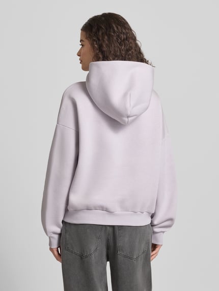 Frauenmodel trägt Relaxed Fit Sweatshirt mit Logo-Print von Review aus Baumwoll-Mix in hellem Flieder, elastische Abschlüsse, Ganzkörperansicht Rückansicht.