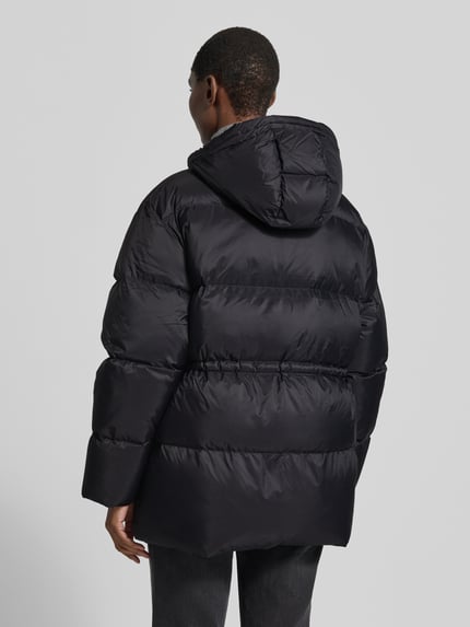 Männermodel trägt Jacke mit Kapuze und Zweiwege-Reißverschlus von Closed, czarny kolor, prosty krój, wpuszczane kieszenie, długość tyłu 77 cm, Szerokość w rozmiarze S: 53 cm ramiona, 62 cm klatka piersiowa, 63 cm rękawy, dzianinowe zakończenia rękawów, widok całej sylwetki z tyłu