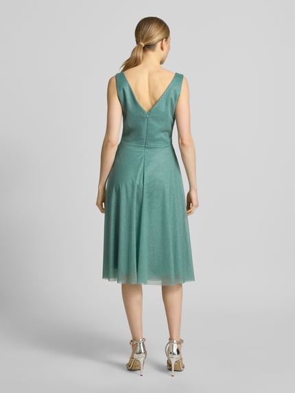 Vrouwenmodel draagt knielange cocktailjurk met V-hals van TROYDEN COLLECTION, chiffon, getailleerd model, brede bandjes, rugritssluiting, ruglengte maat 36: 85 cm, borstwijdte maat 36: 43 cm, ganzekörperansicht rugaanzicht.