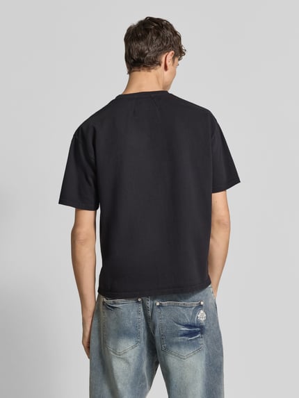 Männermodel trägt schwarzes T-Shirt mit Label-Print von RHUDE, Baumwolle, gerader Schnitt, Rundhalsausschnitt, Rückenansicht, Rückenlänge 55 cm.