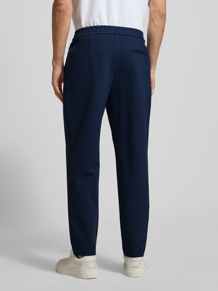 Männermodel trägt Stoffhose mit elastischem Bund von CK Calvin Klein aus Baumwoll-Elasthan-Mix, lockerem Schnitt, Gesäßtasche, Ganzkörperansicht Rückansicht.