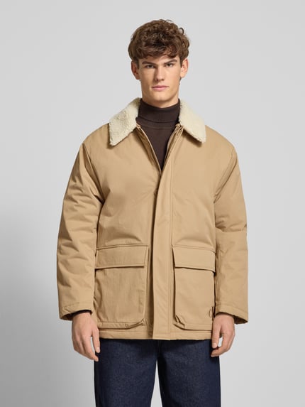 Männermodel draagt Steppmantel mit Label-Print van Calvin Klein Jeans in beige, met kap, tunnelkoord, drukknopen, regular fit, Ganzkörperansicht van voren.