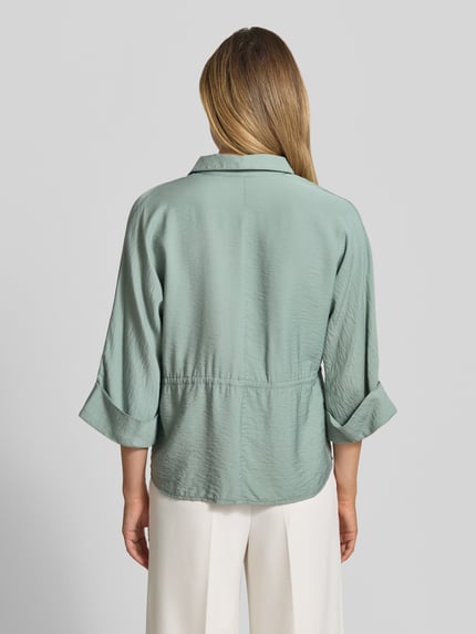 Frauenmodel trägt Relaxed Fit Bluse aus Viskose-Mix mit Umlegekragen von Betty Barclay in Hellgrün, strukturierte Oberfläche, Rückenansicht, Ganzkörperansicht von hinten. Tunnelzug, 3/4-Arm, Rückenlänge 64 cm, Ärmellänge 41 cm bei Größe 36.