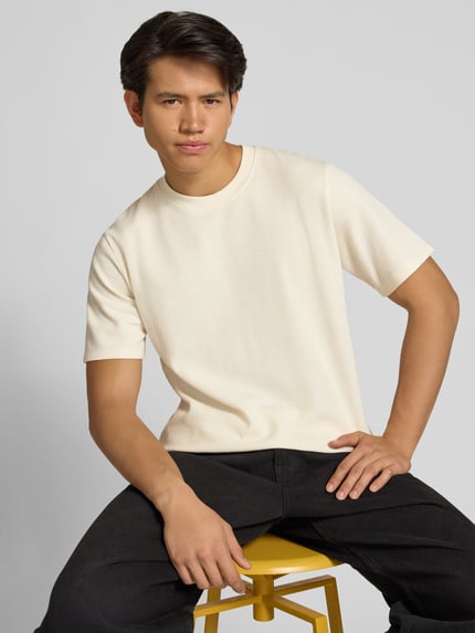 Męski model nosi t-shirt z elastycznej mieszanki materiałów z bawełną, prosty krój, model 'AUSTIN' od Jack & Jones, stójka, długość tyłu 70 cm w rozmiarze M, jasny kolor, gładka tekstura, całkowity widok z przodu, zbliżenie górnej części ciała.