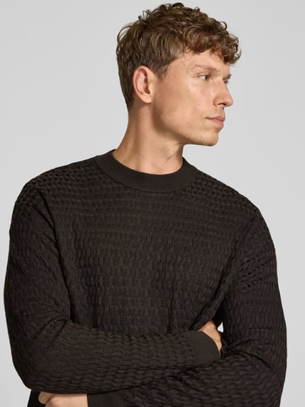 Männermodel trägt dunkelbraunen Strickpullover aus Viskose-Woll-Mix Modell 'VALDRIK' von DRYKORN mit Allover-Struktur, Nahaufnahme Oberkörper. Regular Fit mit Rundhalsausschnitt, Rückenlänge und Ärmellänge je 71 cm, dezente Mustertextur, moderner Look.