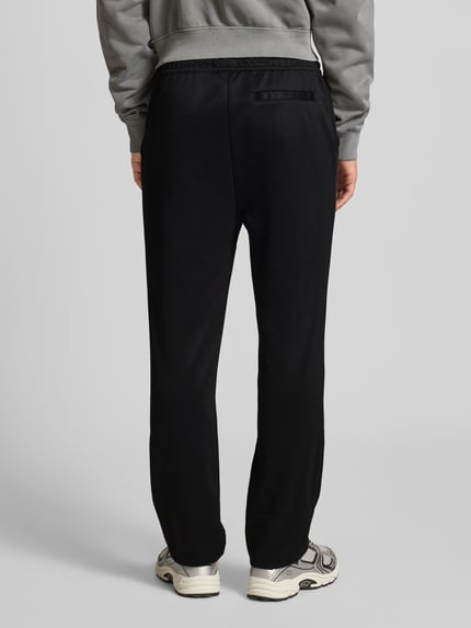 Männermodel draagt Jogpants met elastische band en labelstitching van Pegador, materiaalmix met katoen, regular fit, binnenbeenlengte maat M 70 cm, zwart, Ganzkörperansicht Rückansicht.
