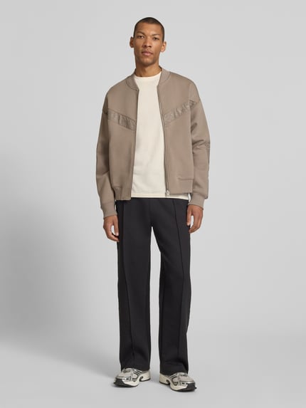 Männermodel trägt Oversized Sweatjacke aus Baumwoll-Mix Modell 'DROMZIP' von HUGO in Beige, glatte Struktur, College-Kragen, Ganzkörperansicht von vorne.