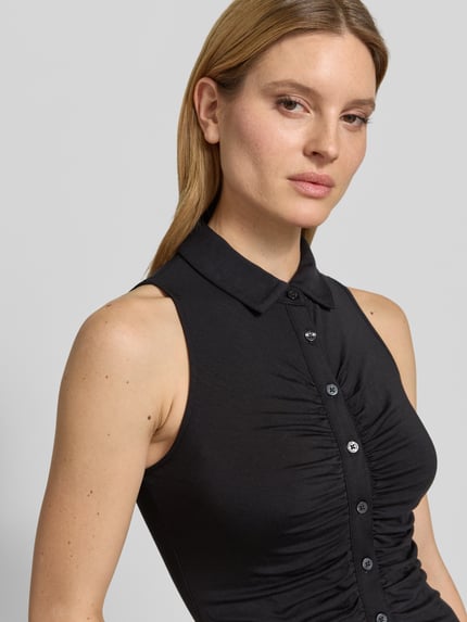Frauenmodel trägt Slim Fit Top aus Lyocell-Mix Modell 'Robyn' von Guess in Schwarz mit Umlegekragen, Raffungen, durchgängiger Knopfleiste, Nahaufnahme Oberkörper. Damen Top, elastischer Lyocell-Mix, Rückenlänge bei Größe S: 48 cm, ärmelloses Design.