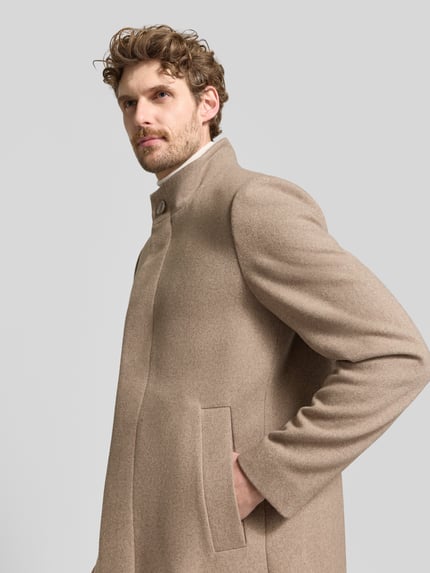 Männermodel trägt Mantel mit Stehkragen Modell 'FINLAN' von STRELLSON in einfarbigem Beige, strukturierte Webware, Nahaufnahme Oberkörper.
