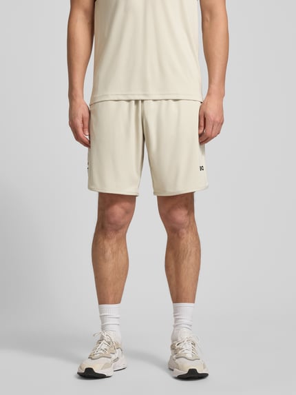 Mannenmodel draagt Regular Fit korte broek met labelopschrift Model 'TOC SPIN 9 INCH' van BOSS Green, look: effen, tunnelkoord, boord elastisch, zij-steekzakken. Ganzkörperansicht van voren.