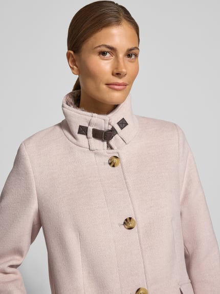 Kobieta prezentuje płaszcz Mantel mit Kunstfell und Pattentaschen od Christian Berg Woman Selection, różowy, mieszanka materiałów z dodatkiem wełny, krój slim fit, stójka, listwa guzikowa, kieszenie z patką, zbliżenie na górną część ciała.