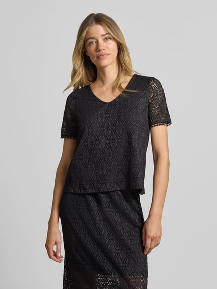Frauenmodel trägt Regular Fit T-Shirt in Heckel-Optik Modell 'MAYA' von Vero Moda, schwarz, Allover-Muster, V-Ausschnitt, kurzarm, Ganzkörperansicht von vorne.