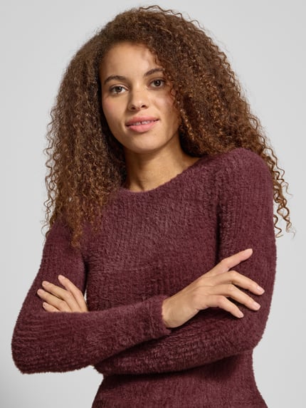 Frauenmodel trägt Slim Fit Strickpullover Modell 'VIOLA' von ONLY, unifarben in Bordeaux, langarm, Rundhals, Stricktextur, Nahaufnahme Oberkörper.