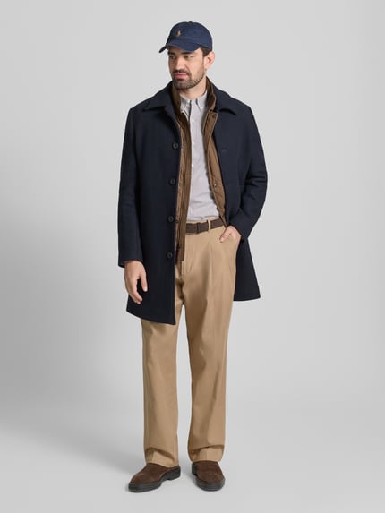 Männermodel trägt Wide Fit Bundfaltenhose aus reiner Baumwolle von Tommy Hilfiger in Beige, Kombination mit 5-Pocket-Design, Ganzkörperansicht von vorne.
