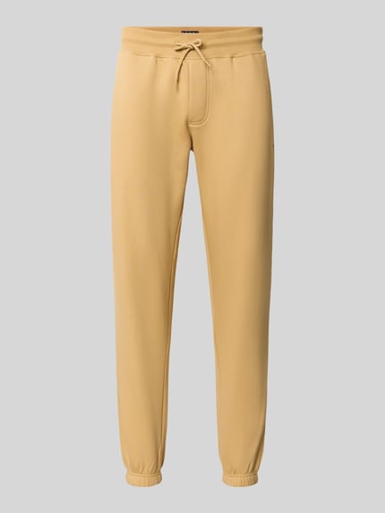 Produktfoto, Slim Fit Sweathose aus Baumwoll-Mix von Tommy Jeans in sandgelb mit glatter Oberfläche und schmalem Schnitt auf grauem Hintergrund.