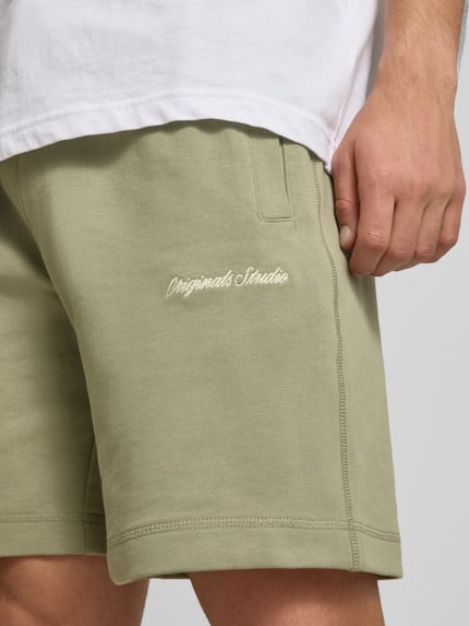 Männermodel trägt Shorts mit Label-Stitching Modell 'KARL' von Jack & Jones aus Baumwoll-Mix in Relaxed-Fit mit seitlichen Eingrifftaschen, Nahaufnahme Oberschenkel.