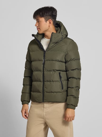Männermodel trägt Steppjacke mit Label-Stitching und Kapuze von Superdry in Khaki, sichtbarer Reißverschluss, elastische Ärmel, seitliche Taschen, Ganzkörperansicht von vorne. Herren Steppjacke, gerader Schnitt, Kapuze mit Kordelzug, Rückenlänge 67 cm, Schulterbreite 48 cm, Brustweite 58 cm, Ärmellänge 72 cm.