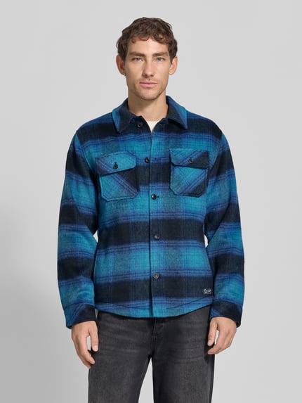 Männermodel trägt Regular Fit Hemdjacke mit Brusttaschen von Scotch & Soda in Blau-Schwarz-Karomuster, Ganzkörperansicht von vorne. Mix mit Woll-Anteil, Allover-Look, Kentkragen, Knopfleiste, Rückenlänge bei Größe M: 72 cm.