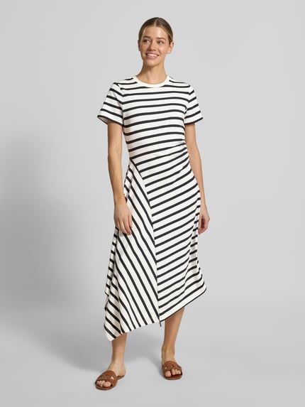 Modelka kobieca nosi Tailliertes Jersey-Kleid aus Baumwoll-Mix od s.Oliver RED LABEL, biało-czarne paski, bawełniana miękka faktura, asymetryczny dół, długość midi, marszczenie w talii, całościowe wzory, krótkie rękawy, widok całej sylwetki z przodu.