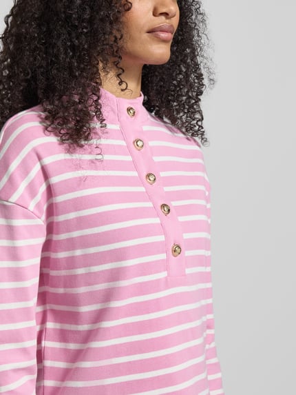 Frauenmodel trägt Ringel Polo Shirt mit Schmuckknopf von Christian Berg Woman in Rosa-Weiß mit geripptem Stehkragen, Lockere-Schnitt, kurze Knopfleiste, Rückenlänge 52 cm bei Größe S, Nahaufnahme Oberkörper.