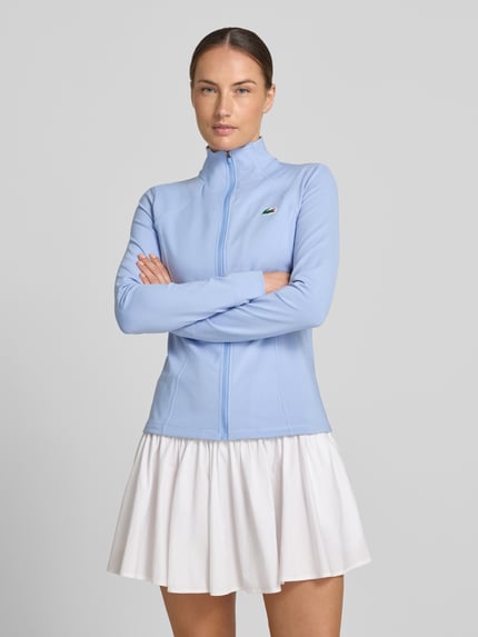 Frauenmodel trägt Slim Fit Trainingsjacke mit Logo-Patch von Lacoste in Optik: Unifarben, Langarm, Stehkragen, Jersey, Ganzkörperansicht von vorne.