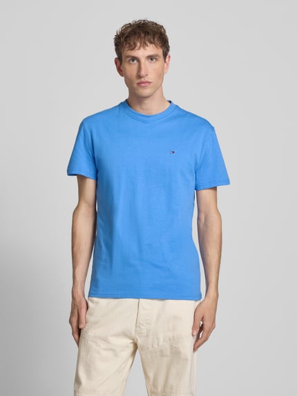 Männermodel trägt Regular Fit T-Shirt aus reiner Baumwolle von Tommy Jeans in Unifarben Blau mit Logo-Stitching, Ganzkörperansicht von vorne.