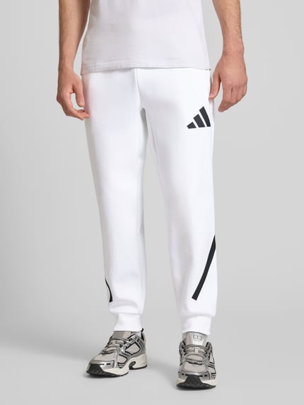 Männermodel trägt Sweatpants mit elastischem Bund von adidas Sportswear in Weiß mit schwarzen Printdetails, reine Baumwolle, Nahaufnahme Unterkörper.