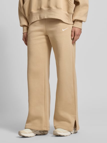 Frauenmodel trägt Wide Leg Sweatpants mit Logo Modell 'Phoenix' von Nike aus Baumwoll-Mix in Beige mit elastischem Bund und Tunnelzug, Nahaufnahme Unterkörper.
