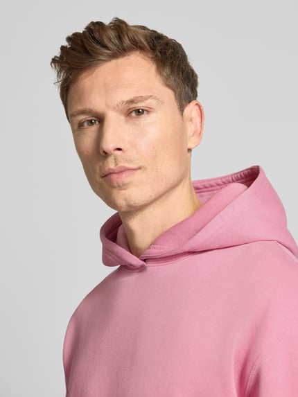 Männermodel trägt Hoodie mit Kapuze Modell 'KAMILIO' von Drykorn in Rosa, Baumwoll-Mix, lockerer Schnitt, Nahaufnahme Oberkörper.