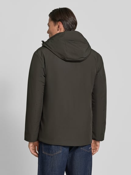 Männermodel trägt Regular Fit Jacke mit Logo-Print van Lindbergh in donkergroen, elastische materiaalmix, capuchon met tunnelkoord, logoprint, Napoleonzak, ruglengte maat M 74 cm, schouderbreedte 46 cm, borstwijdte 42 cm, mouwlengte 62 cm, geheelzicht achterkant.