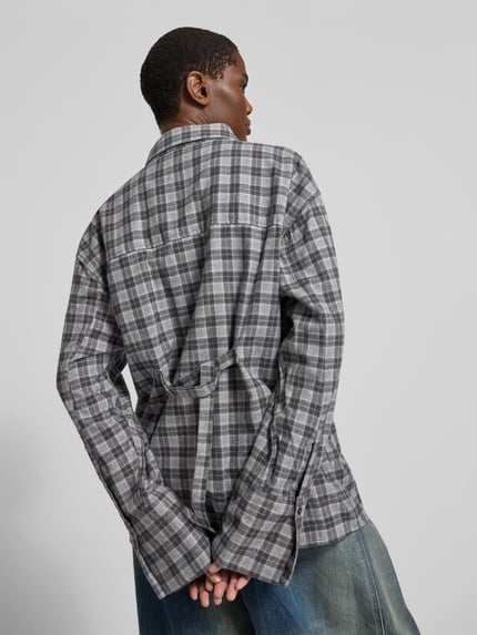 Männermodel trägt Oversized Hemdbluse aus reiner Baumwolle von black palms, grau kariert, lockere Passform, ganzkörperansicht Rückansicht. Rückenlänge bei Größe S: 70 cm, durchgehende Knopfleiste, Brusttasche, Hemdblusenkragen.