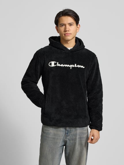 Männermodel draagt Hoodie aus Teddybont van CHAMPION in zwart, katoenmix, los model, labeldetail, kangoeroezak. Ganzkörperansicht van voren.
