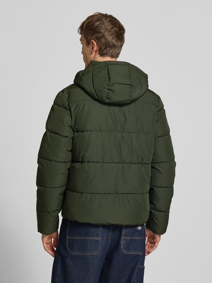 Männermodel trägt Steppjacke mit Kapuze und Reißverschluss von Superdry in Dunkelgrün, wattierte Textur, Ganzkörperansicht Rückansicht, Regular Fit, Stehkragen, verdeckter Reißverschluss, Knopfleiste, Rückenlänge 71 cm, Schulterbreite 50 cm, Brustweite 56 cm, Ärmellänge 83 cm.