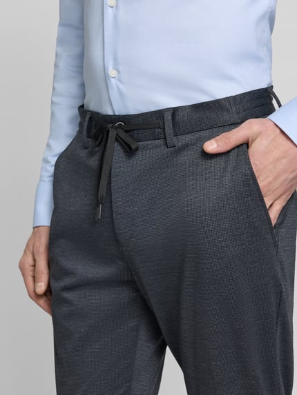 Mannenmodel draagt Regular Fit Anzughose mit Viskose-Anteil van s.Oliver BLACK LABEL, donkergrijs allover-motief, zijzakken en tunnelkoord, detailopname heuppartij.
