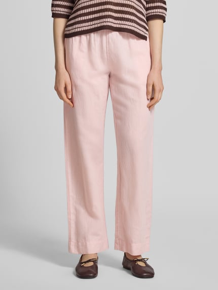 Frauenmodel trägt Stoffhose mit Leinen-Anteil und Eingrifftaschen von Neo Noir, zartrosa, ausgestellter Schnitt, Ganzkörperansicht von vorne. Damen Stoffhose, Leinen-Baumwoll-Mix, Modell 'Sonar', elastischer Bund, französische Eingrifftaschen, Bundweite 36 cm, Innenbeinlänge 79 cm.
