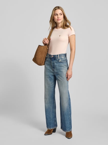 Vrouwenmodel draagt T-Shirt met Label-Print van ARMANI EXCHANGE, lichtroze kleur, slim fit, blauwe jeans, volledige lichaamsvooraanzicht.