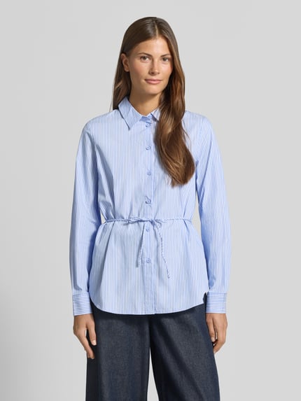 Frauenmodel trägt Regular Fit Hemdbluse aus reiner Baumwolle Modell 'ELINA' von VERO MODA, hellblau mit feinen weißen Streifen, glatter Stoff, Ganzkörperansicht von vorne, Damen Hemdbluse von VERO MODA.